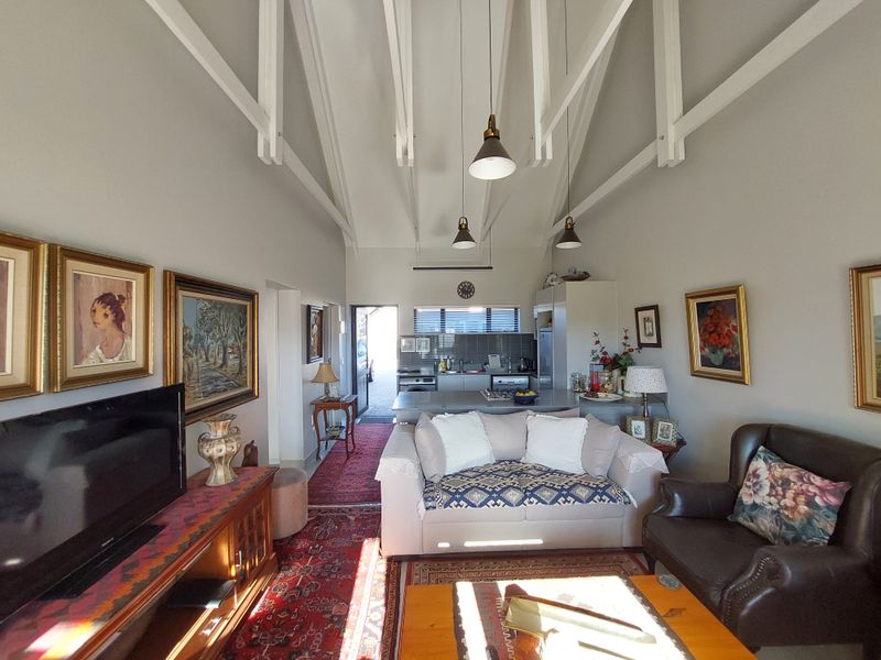 An open-plan living and kitchen area featuring high vaulted ceilings with exposed rafters, pendant lighting, and a functional kitchen layout with built-in appliances.