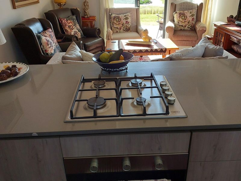 Open plan kitchen featuring a stone-topped island with a built-in gas hob and oven, overlooking a bright living area with sliding door access.