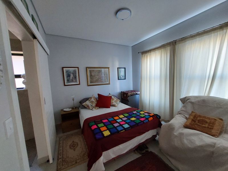 A functional bedroom featuring neutral wall tones, a sliding door entrance, and large windows with fitted curtain tracks for natural light.