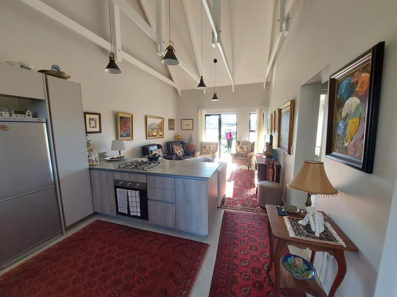 Spacious open-plan living area featuring a modern kitchen island with gas hob, vaulted ceilings with exposed rafters, and direct access to the outdoor area.