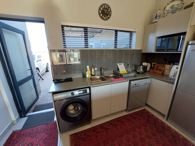 A functional scullery featuring modern cabinetry, a double basin sink, tiled splashback, and integrated appliances, with direct access to the exterior.