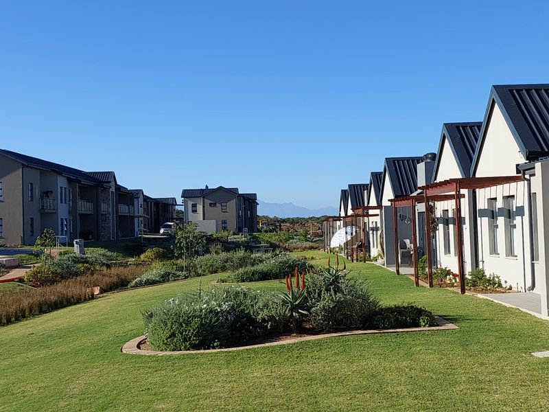 A view of the retirement village grounds featuring well-maintained landscaped gardens, paved pathways, and modern residential units with timber pergolas.