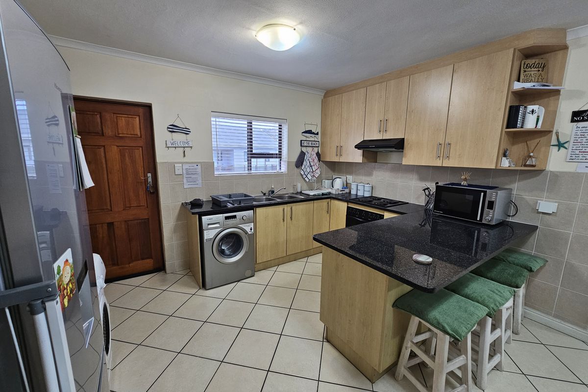 Functional kitchen featuring light wood cabinetry, granite countertops, tiled backsplash, and integrated appliances, including a built-in oven and hob.