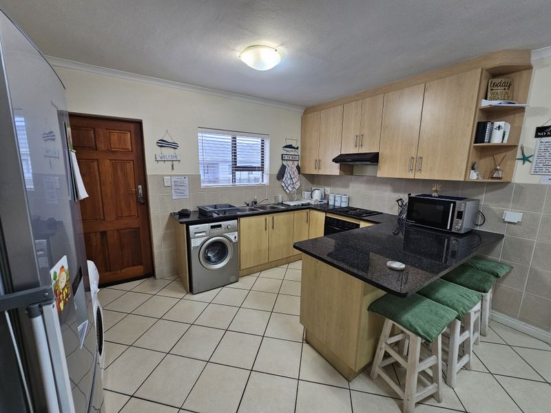 Functional kitchen featuring light wood cabinetry, granite countertops, tiled backsplash, and integrated appliances, including a built-in oven and hob.