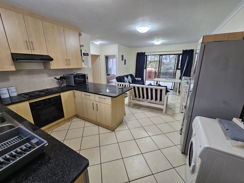 Open-plan kitchen and living area featuring light wood cabinetry, granite countertops, tiled flooring, and direct access to a patio through sliding glass doors.