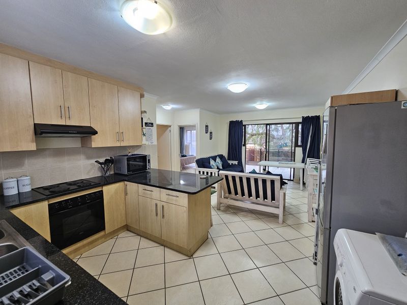 Open-plan kitchen and living area featuring light wood cabinetry, granite countertops, and ceramic floor tiles, leading to a balcony through sliding glass doors.