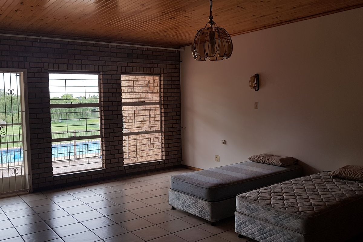 Spacious bedroom featuring exposed brick walls, timber-clad ceiling, tiled flooring, and direct access to an outdoor balcony overlooking the pool area.