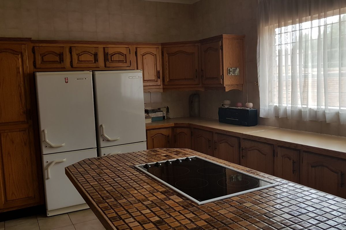 A traditional kitchen featuring wooden cabinetry, a tiled island countertop with an integrated electric hob, and ample storage space.