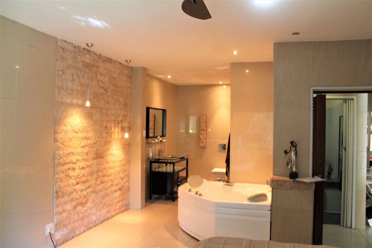 A spacious bathroom featuring a corner spa bathtub, a textured stone feature wall, recessed lighting, and tiled flooring.