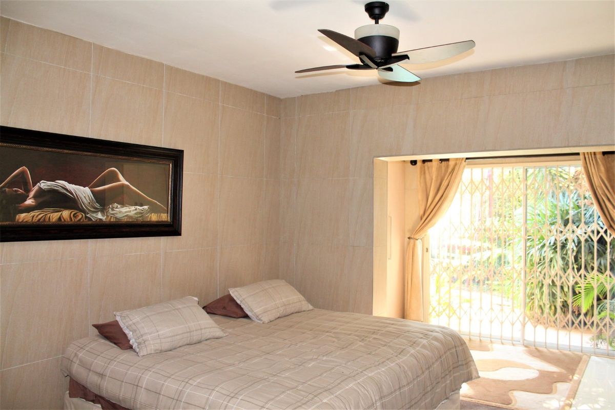 A bedroom featuring tiled walls, a ceiling fan, and sliding glass doors with security gates leading to an outdoor area.