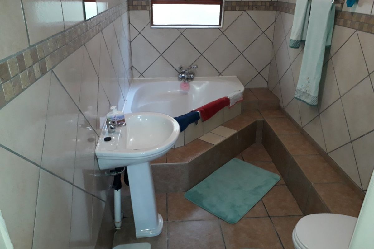 A functional bathroom featuring a corner bathtub, pedestal basin, and toilet with neutral tiled finishes.
