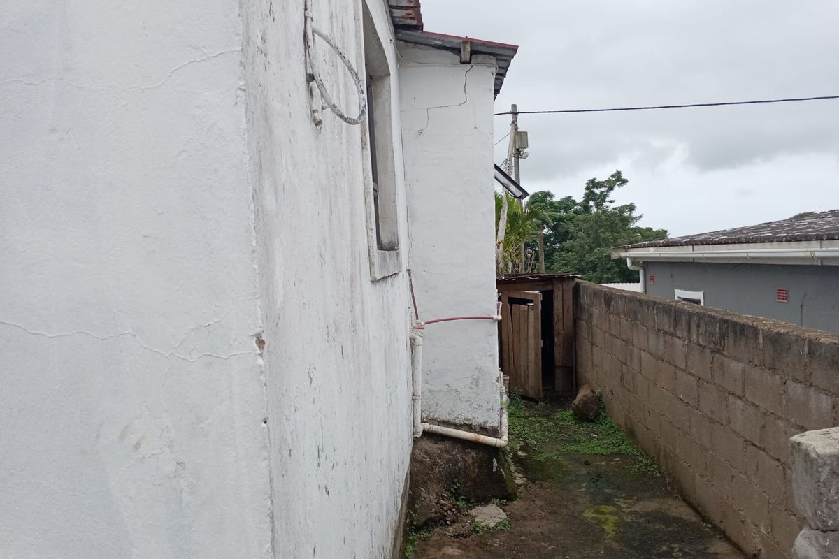 Side exterior view of the property showing a narrow walkway, concrete block boundary wall, and visible structural cracking on the exterior wall.