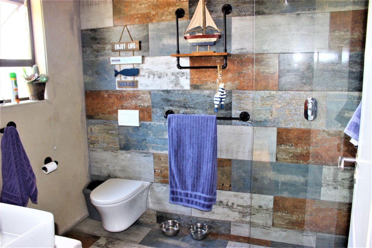 Modern bathroom featuring multi-tonal wood-look wall tiles, a wall-mounted toilet, and a glass-enclosed shower area with industrial-style fixtures.