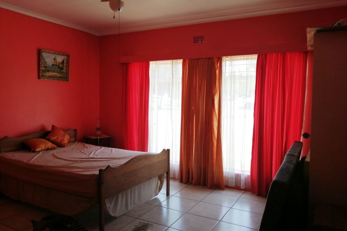 A bedroom featuring tiled flooring, a ceiling fan, and large windows covered by curtains, providing natural light to the space.