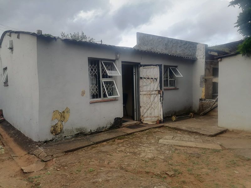 Rear exterior view of a single-story dwelling showing weathered plaster, security gates, and concrete ground surfacing requiring maintenance and repair.