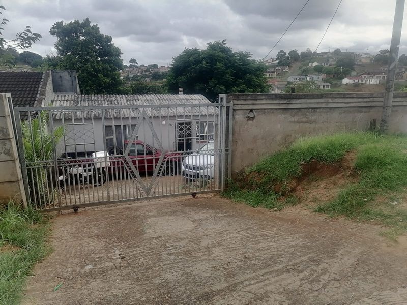 Front view of the property featuring a metal sliding gate, concrete driveway, and perimeter boundary wall with a tiled roof dwelling.