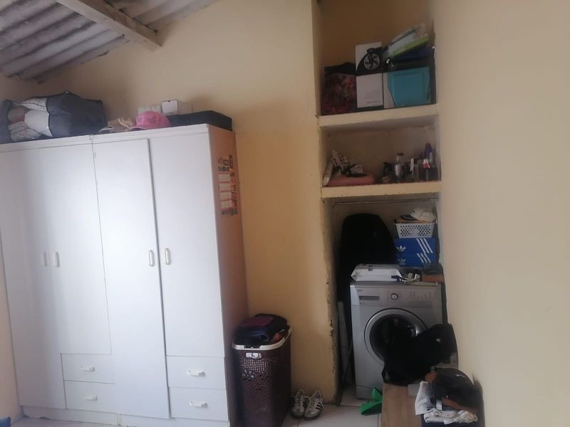 A functional laundry area featuring built-in shelving and exposed ceiling rafters, providing practical utility space with potential for cosmetic improvement.