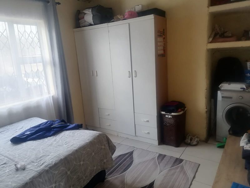A bedroom featuring tiled flooring, a built-in wardrobe, and a recessed shelving area, with security bars installed on the window.