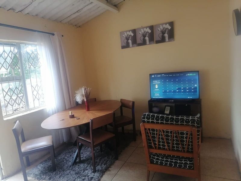 A living area featuring tiled flooring, exposed ceiling beams, and a security gate on the window, offering a functional space with potential for cosmetic updates.