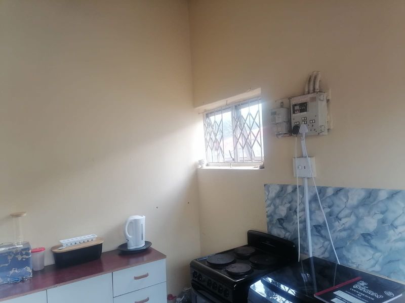 A functional kitchen area featuring built-in cabinetry, an electric stove, and a tiled splashback, with visible electrical infrastructure and security bars on the window.