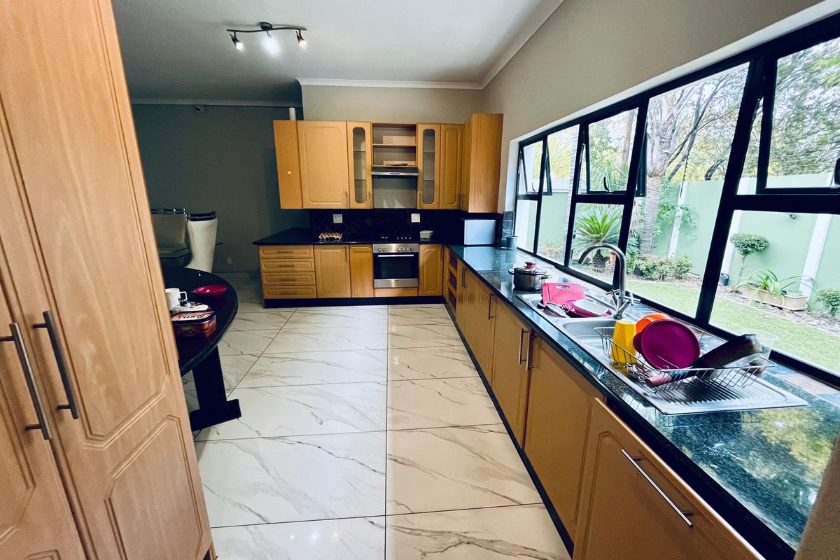 A spacious kitchen featuring light wood cabinetry, dark granite countertops, and large marble-look floor tiles, with a large window overlooking the garden.