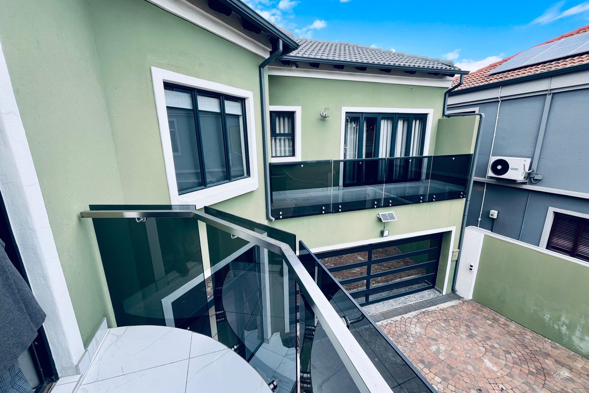 Rear view of the property featuring a modern glass balustrade balcony, paved driveway, and garage access.