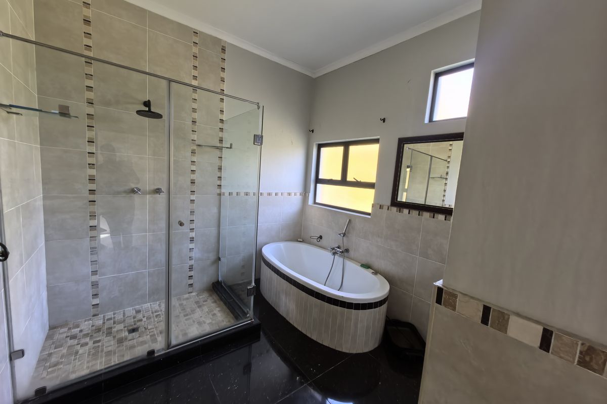 Modern bathroom featuring a freestanding bathtub, a spacious glass-enclosed shower, and neutral wall tiling with decorative accents.