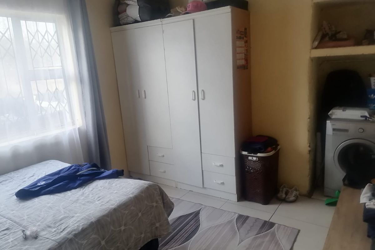 A bedroom featuring tiled flooring, a built-in wardrobe, and a recessed shelving area, with security bars installed on the window.