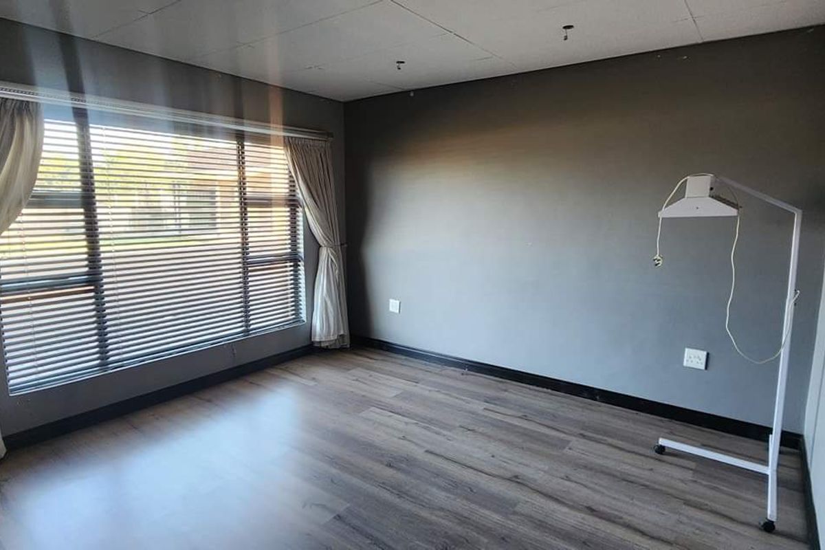 A spacious, neutral-toned room featuring wood-look laminate flooring, large windows with blinds, and a drop ceiling, suitable for use as a bedroom or office.