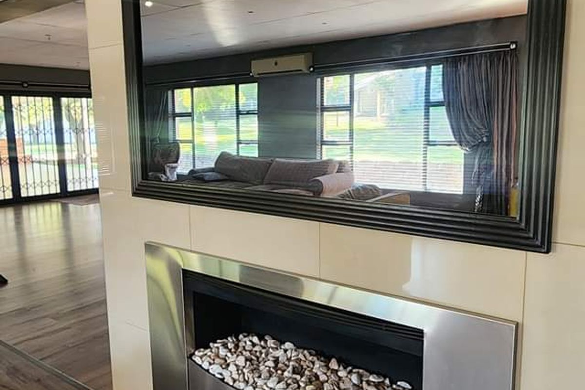 A modern living room feature wall showcasing a built-in stainless steel fireplace with stone detailing and a large decorative wall mirror.