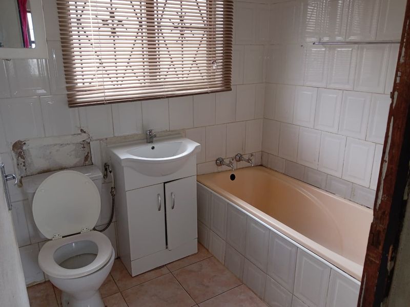 A functional bathroom featuring a built-in vanity, bathtub, and tiled finishes, currently requiring cosmetic updates and repairs to the wall area.