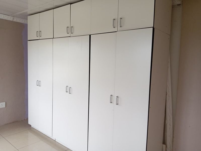 A bedroom featuring floor-to-ceiling white built-in cupboards and tiled flooring, providing ample storage space.