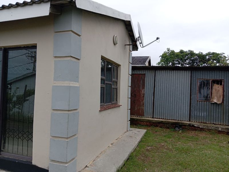 Rear view of the property showing a main structure with sliding doors and an adjacent corrugated metal outbuilding in the backyard.