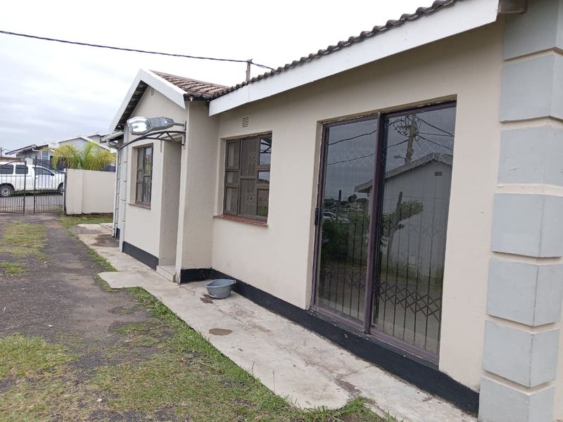 Rear exterior view of the house featuring a sliding glass door with security bars, tiled roof, and a concrete pathway along the building perimeter.