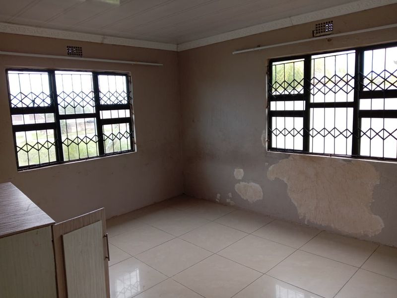 An empty bedroom featuring tiled flooring, security bars on windows, and built-in cabinetry, requiring cosmetic wall repairs and repainting.