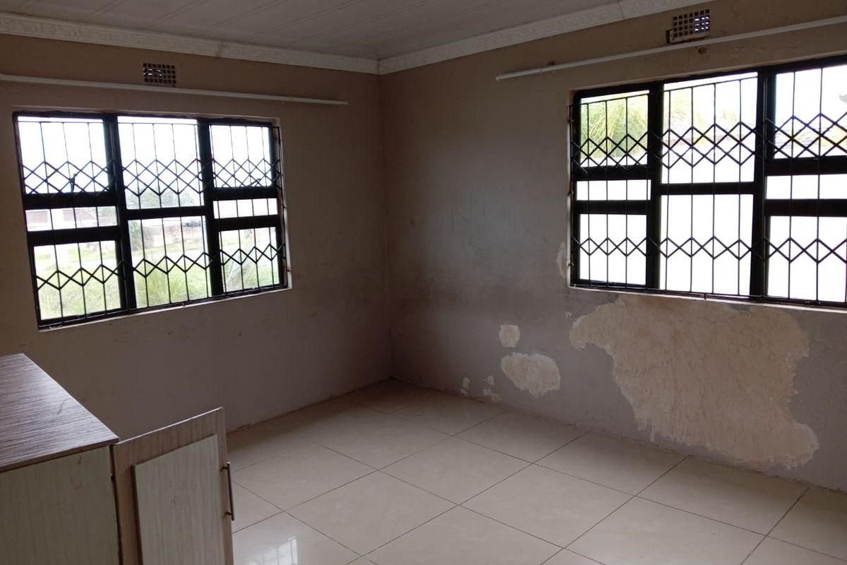 An empty bedroom featuring tiled flooring, security bars on windows, and built-in cabinetry, requiring cosmetic wall repairs and repainting.