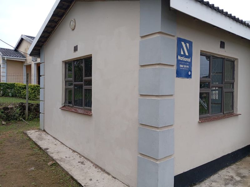 Exterior view of the property featuring plastered walls, aluminium window frames with security bars, and a concrete apron surrounding the building.