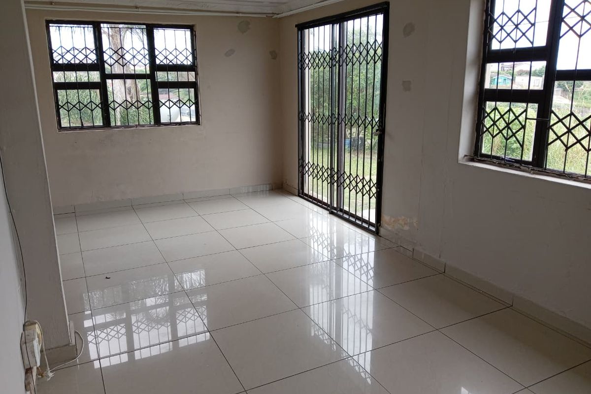 An empty living room featuring tiled flooring, security bars on windows, and a sliding security gate leading to the exterior.