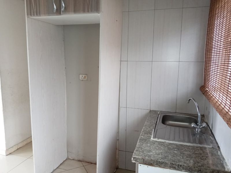 A compact kitchen area featuring a stainless steel sink, tiled splashback, and a dedicated alcove for a refrigerator.