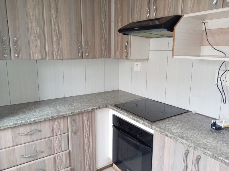 A functional kitchen featuring wood-look laminate cabinetry, granite countertops, a built-in oven, electric hob, and an extractor fan with tiled backsplash.