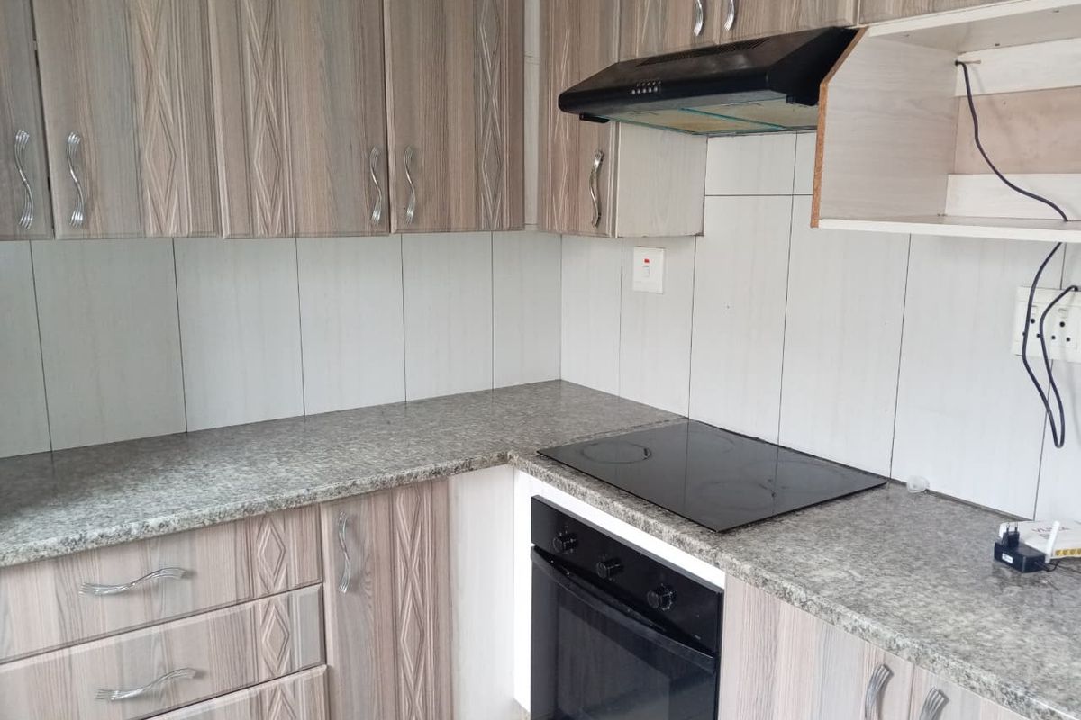 A functional kitchen featuring wood-look laminate cabinetry, granite countertops, a built-in oven, electric hob, and an extractor fan with tiled backsplash.