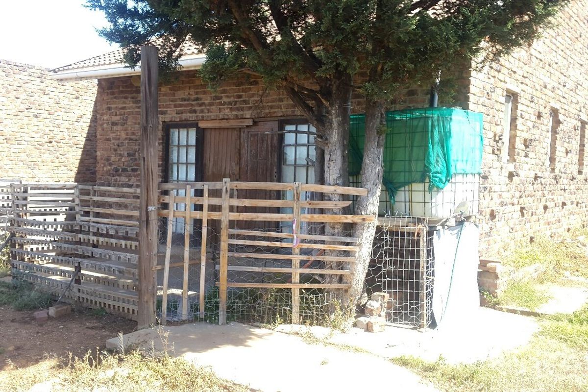 Exterior view of a rustic brick farm building featuring a small fenced patio area and an external water storage tank.