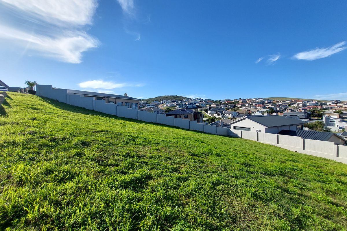 A view of a sloped, vacant residential plot featuring a perimeter boundary wall and surrounding neighborhood views.