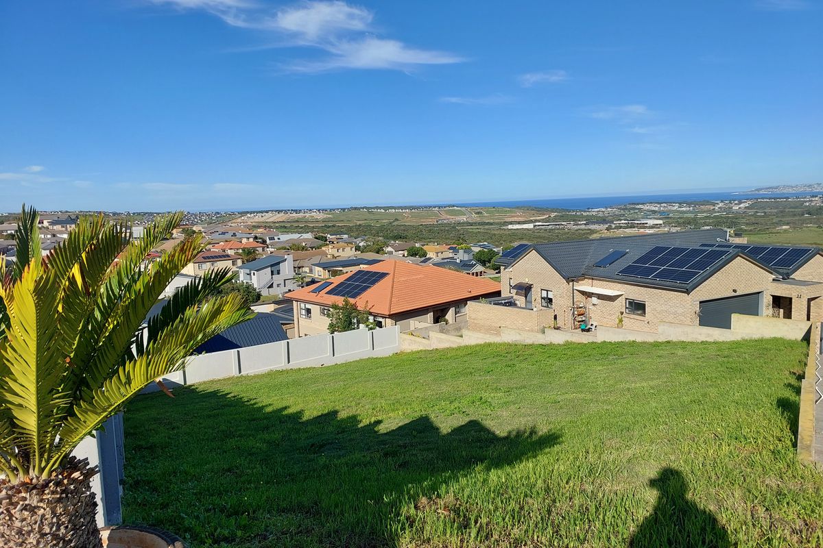 Elevated view overlooking a residential neighborhood with coastal landscape in the distance, featuring a sloped grass plot in the foreground.