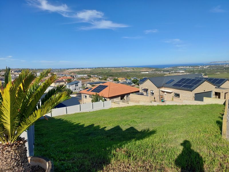 Elevated view overlooking a residential neighborhood with coastal landscape in the distance, featuring a sloped grass plot in the foreground.