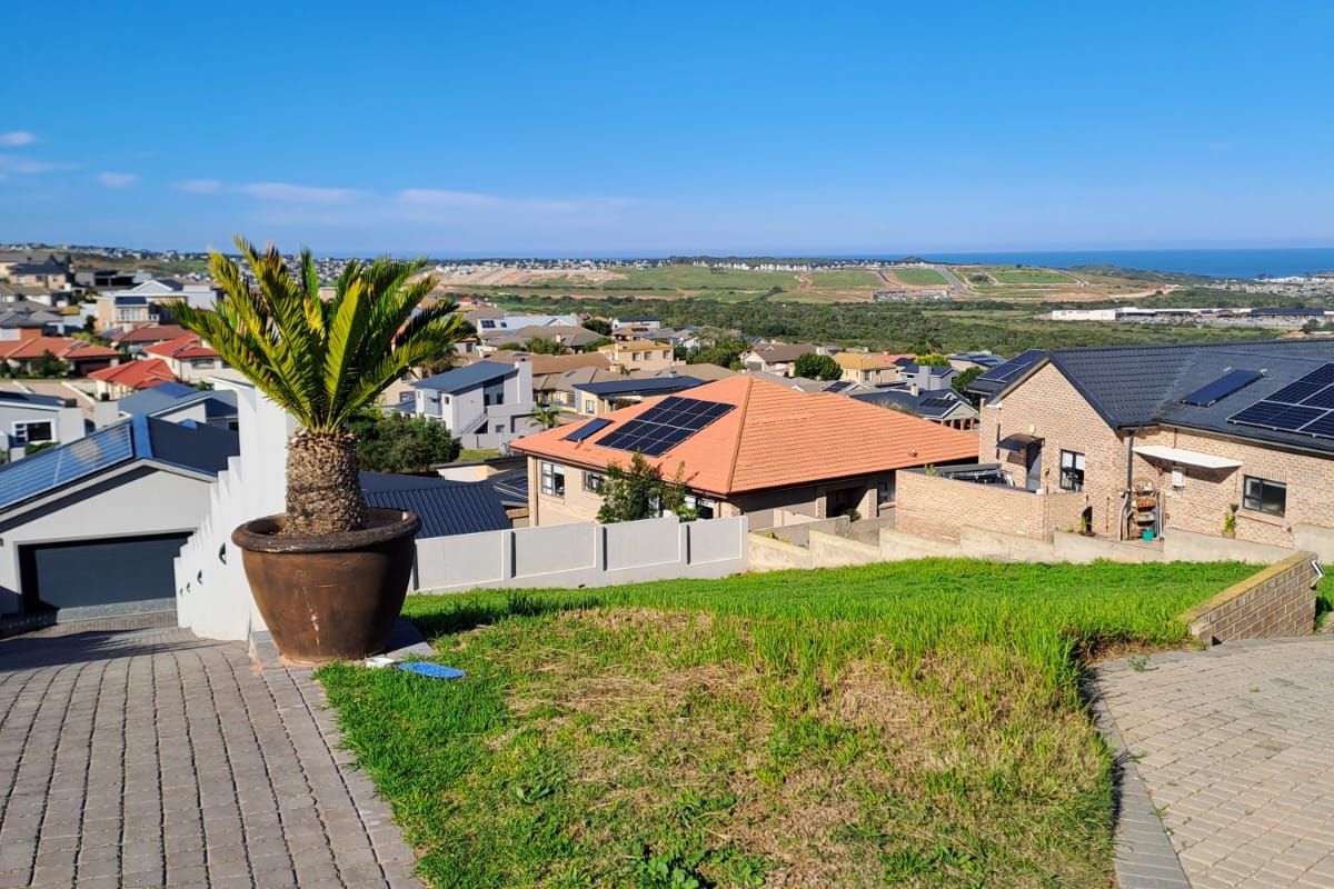 Elevated view overlooking a residential neighborhood with coastal scenery in the distance, featuring paved driveway access and established landscaping.