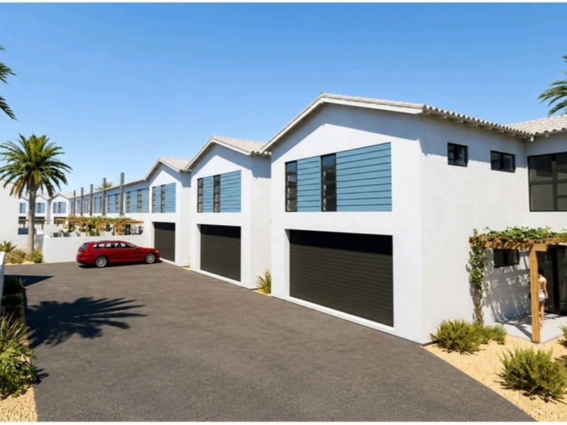 A modern townhouse complex featuring multiple garage bays, clean white facades with blue accent panels, and a paved driveway area.