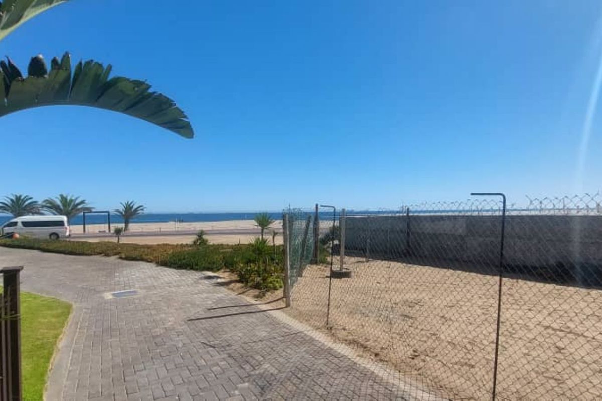A clear view of the coastline and beach area from the property, featuring paved pathways and perimeter fencing.