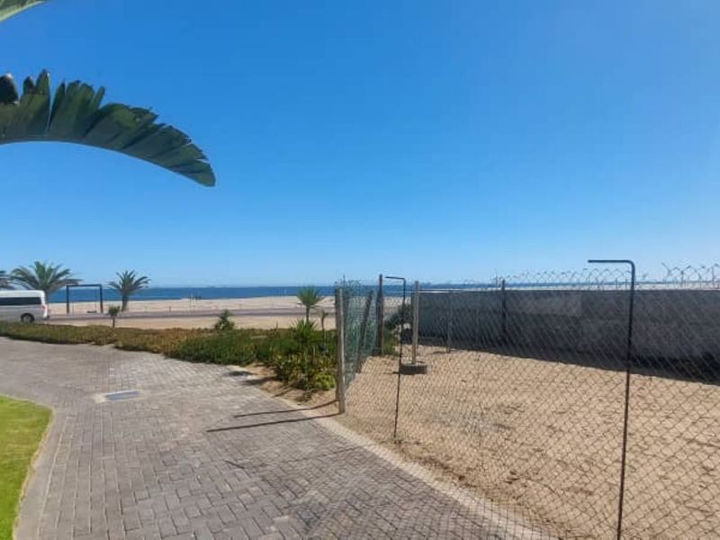 A clear view of the coastline and beach area from the property, featuring paved pathways and perimeter fencing.