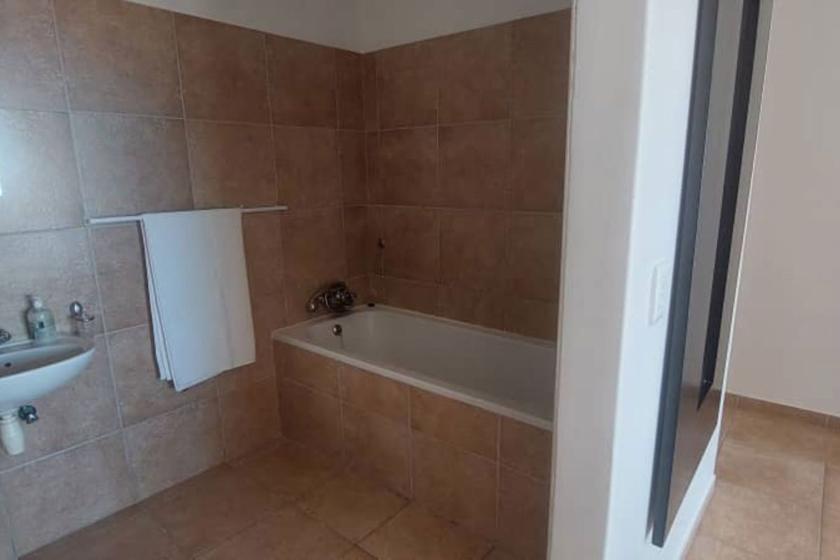 A functional bathroom featuring tiled walls and flooring, a built-in bathtub, and a wall-mounted basin with chrome fixtures.